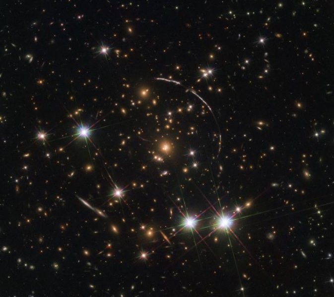 На этом снимке, снятом космическим телескопом Хаббла НАСА / ЕКА, показано массивное скопление галактик, расположенное на расстоянии около 4,6 миллиарда световых лет. Вдоль его границ видны четыре яркие дуги; это копии той же далекой галактики, по прозвищу Арка Солнечных лучей. Предоставлено: ESA / Hubble, NASA, Rivera-Thorsen et al.